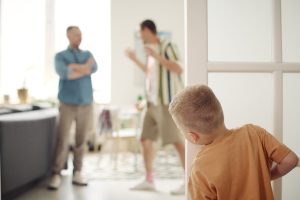 Rear view of little boy looking out from behind door and watching for quarrel of adults