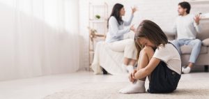 Family Conflict. Little girl crying after parents quarrel at home, sitting alone with her head down, hiding her face in knees, selective focus